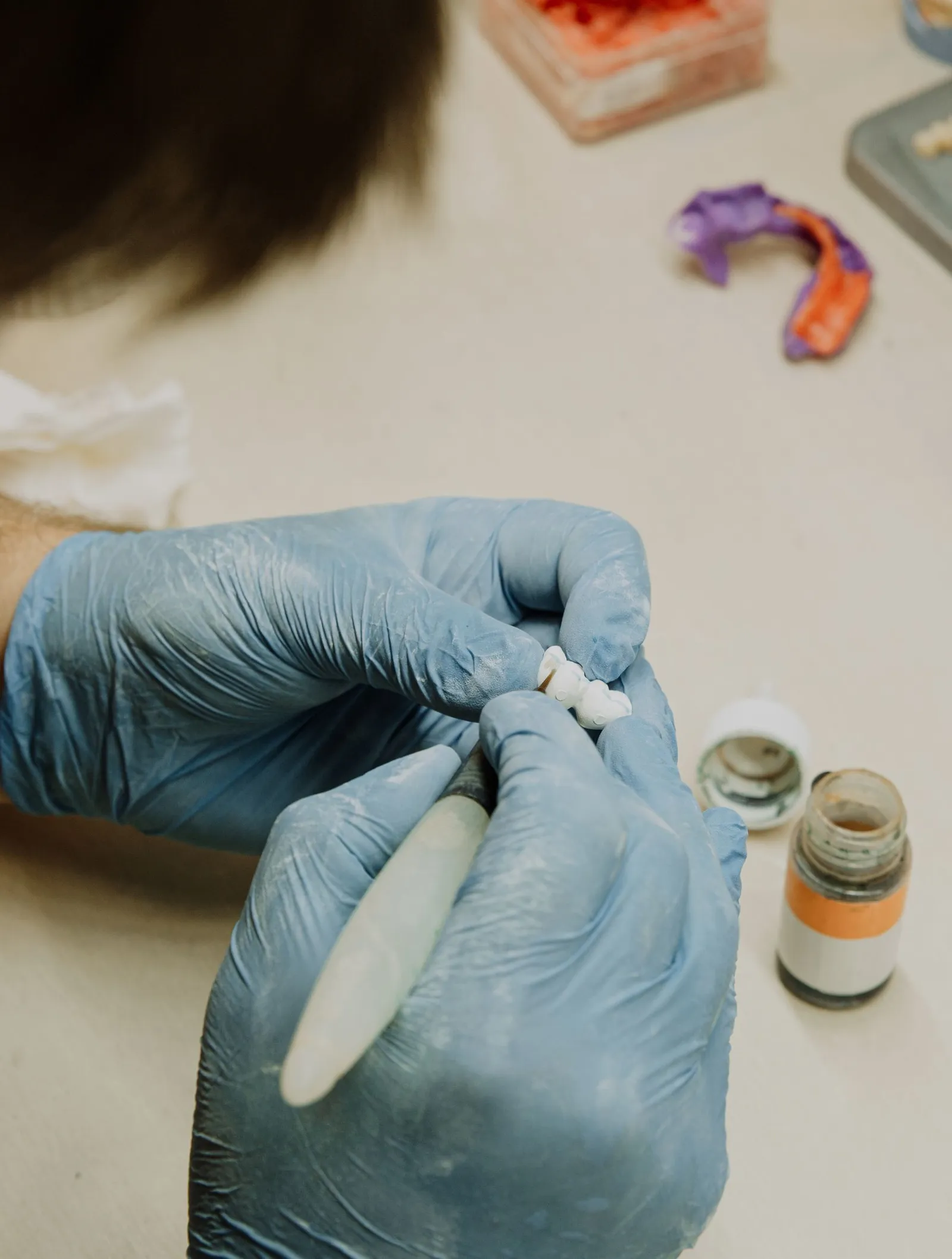 Protésico dental dando forma a una corona de porcelana con guantes