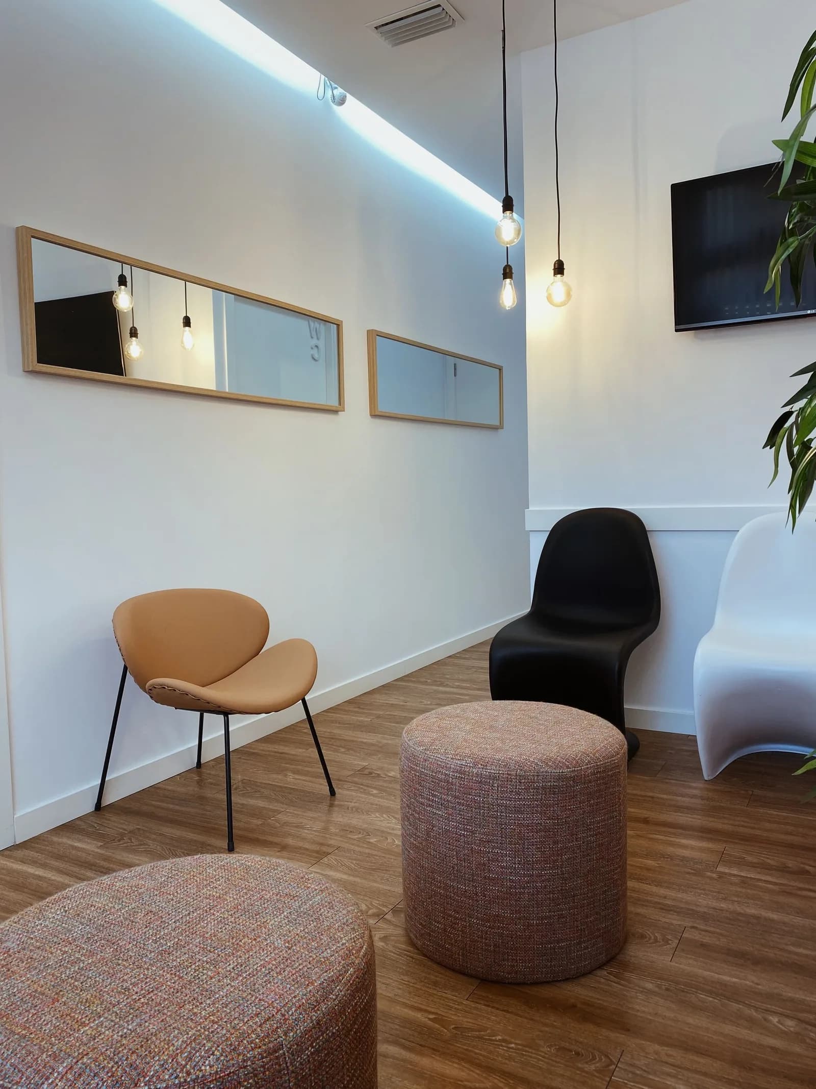 Sala de espera de la clínica, con dos pufs tapizados en rosa, una butaca de piel y espejos de marco de madera